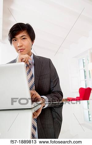 Stock Image - Young Asian man working on his laptop computer. Fotosearch