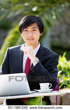 Stock Image - Young Asian man working on his laptop computer outside. Fotosearch