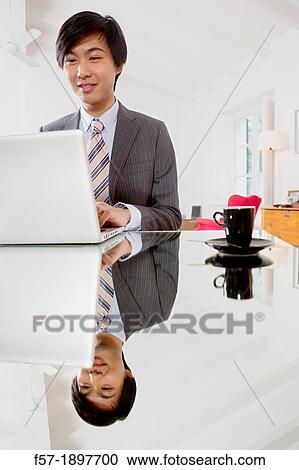 Stock Image - Young Asian man working on his laptop computer. Fotosearch