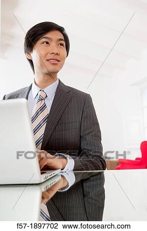Stock Image - Young Asian man working on his laptop computer. Fotosearch