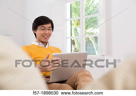 Stock Image - Young Asian man working on his laptop computer. Fotosearch
