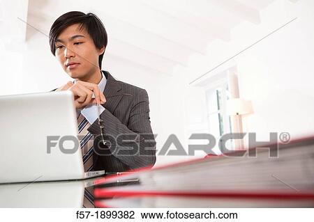 Stock Image - Young Asian man working on his laptop computer. Fotosearch