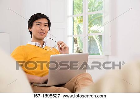Stock Photo - Young Asian man working on his laptop computer. Fotosearch