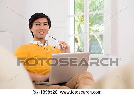Stock Photo - Young Asian man working on his laptop computer. Fotosearch