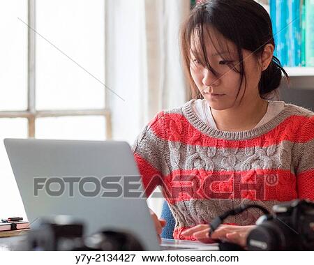 Young Asian woman in casual clothes works at the desk in her home office. View Large Photo Image Stock Photo - Young Asian woman in casual clothes works at the desk in her home office.. Fotosearch
