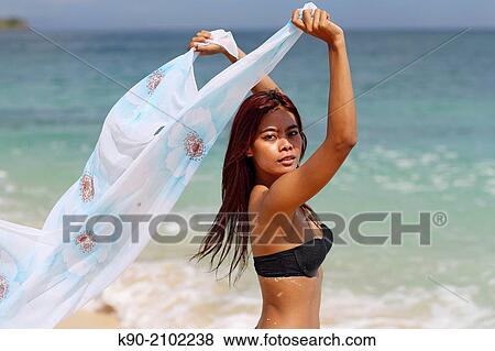 Stock Photo - Young asian woman sitting playing with a whit tissue in the at the beach, Bali, Indonesia, Southeast Asia.. Fotosearch