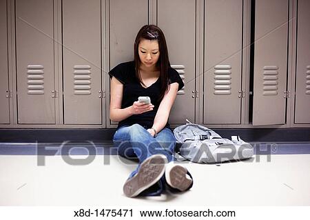Young Asian woman texting on her smart phone while sitting on floor in school hallway. View Large Photo Image Stock Image - Young Asian woman texting on her smart phone while sitting on floor in school hallway.. Fotosearch