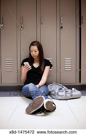 Young Asian woman texting on her smart phone while sitting on floor in school hallway. View Large Photo Image Stock Image - Young Asian woman texting on her smart phone while sitting on floor in school hallway.. Fotosearch