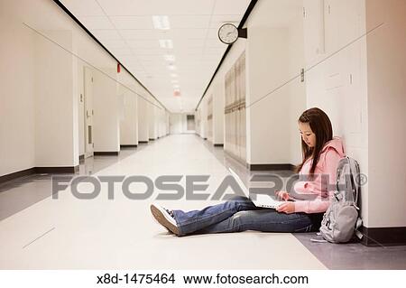 Young Asian woman using her laptop computer while sitting on floor in school hallway. View Large Photo Image Picture - Young Asian woman using her laptop computer while sitting on floor in school hallway.. Fotosearch