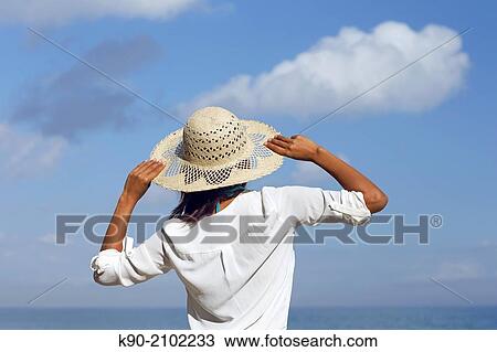 Stock Image - Young asian woman wearing a hat, holding the hat with left and right hand, Bali, Indonesia, Southeast Asia.. Fotosearch