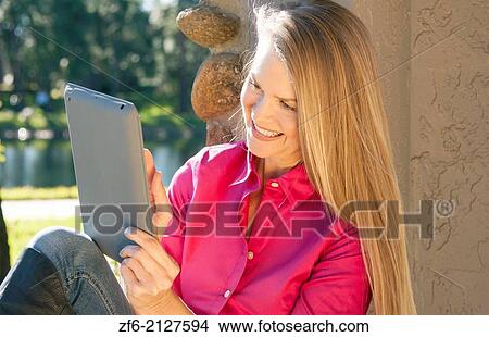 young attractive 50 year old woman playing on ipad tablet smiling outdoors still beautiful even in middle age with sunlight in her hair and great smile. View Large Photo Image Picture - young attractive 50 year old woman playing on ipad tablet smiling outdoors still beautiful even in middle age with sunlight in her hair and great smile.. Fotosearch