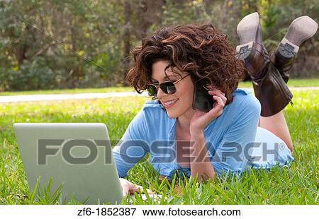 Stock Photo - Young attractive woamn age 25 in front of home in yard emailing and talking on cell to friends with sunglasses and modern look. Fotosearch