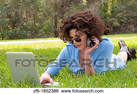 Stock Photograph - Young attractive woamn age 25 in front of home in yard emailing and talking on cell to friends with sunglasses and modern look. Fotosearch