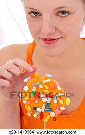 Young beautiful woman about to take a pill from an orange lollipop View Large Photo Image Picture - Young beautiful woman about to take a pill from an orange lollipop. Fotosearch