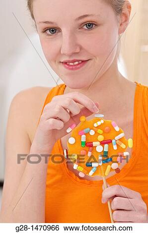 Stock Photograph - Young beautiful woman about to take a pill from an orange lollipop. Fotosearch