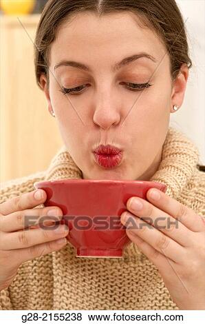 young beautiful woman drinking and blowing to cool a hot drink from a red china bowl, in a beige pull over View Large Photo Image Stock Photo - young beautiful woman drinking and blowing to cool a hot drink from a red china bowl, in a beige pull over. Fotosearch