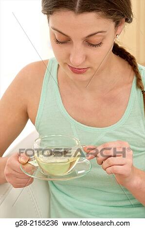 Stock Photograph - young beautiful woman holding a glass cup of herb tea with a slice of lemon, suffering from a cold. Fotosearch