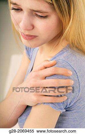 Stock Photography - Young beautiful woman holding her stiff painful shoulder. Fotosearch