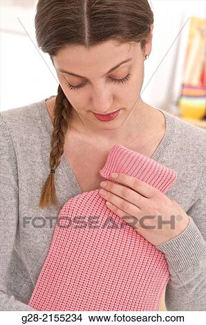Young beautiful woman in grey holding a pink hot water bottle for stomach ache relief View Large Photo Image Picture - Young beautiful woman in grey holding a pink hot water bottle for stomach ache relief. Fotosearch