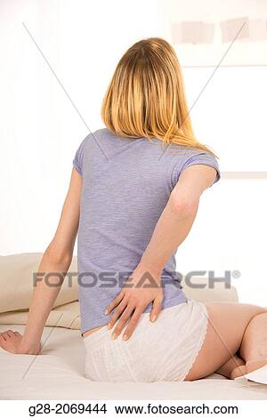 Young beautiful woman sitting on a bed and suffering from back ache View Large Photo Image Picture - Young beautiful woman sitting on a bed and suffering from back ache. Fotosearch