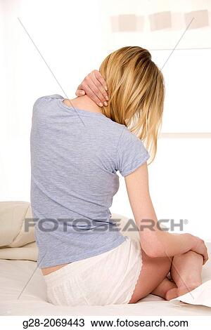 Young beautiful woman sitting on a bed and holding her stiff painful neck View Large Photo Image Stock Image - Young beautiful woman sitting on a bed and holding her stiff painful neck. Fotosearch