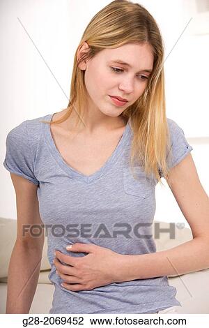 Stock Image - Young beautiful woman sitting on a bed and holding her stomach for pain. Fotosearch