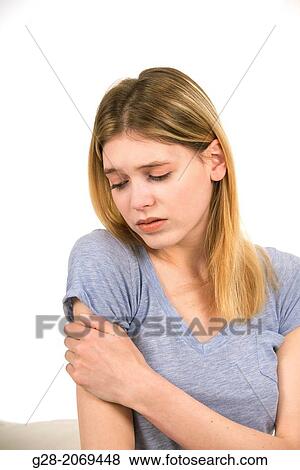 Stock Photo - Young beautiful woman sitting on a bed and holding her stiff painful arm. Fotosearch