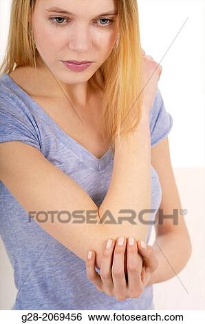 Young beautiful woman sitting on a bed and holding her stiff painful elbow View Large Photo Image Stock Photograph - Young beautiful woman sitting on a bed and holding her stiff painful elbow. Fotosearch