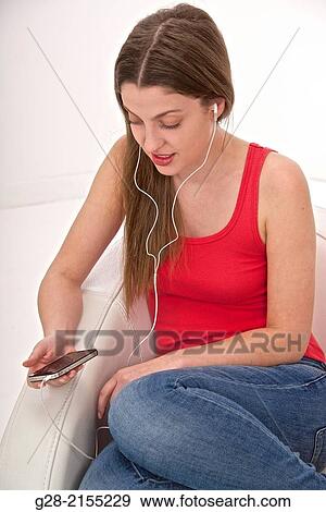 Young beautiful woman using her phone as an I pod and listening to music in a white leather armchair View Large Photo Image Stock Photo - Young beautiful woman using her phone as an I pod and listening to music in a white leather armchair. Fotosearch