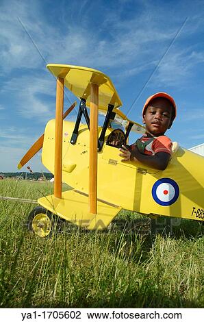 Stock Image - Young black boy sitting in a small biplane Tiger Moth. Fotosearch
