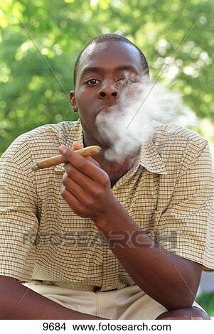 Young black man in a summer shirt blowing cigar smoke View Large Photo Image Picture - Young black man in a summer shirt blowing cigar smoke. Fotosearch
