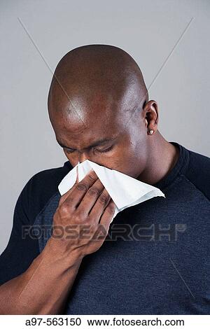 Young black man with shaved head blowing his nose or sneezing into a tissue. View Large Photo Image Stock Image - Young black man with shaved head blowing his nose or sneezing into a tissue.. Fotosearch