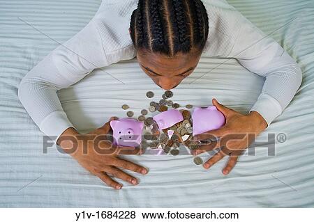 Stock Photo - Young black man with United States coins and a broken piggy bank. Fotosearch