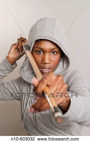 Stock Image - Young black woman pointing a pool cue towards the camera.. Fotosearch