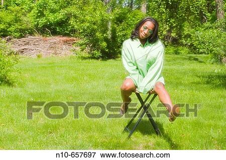 Young black woman, wearing sunglasses, sitting on a stool in her backyard. View Large Photo Image Stock Photo - Young black woman, wearing sunglasses, sitting on a stool in her backyard.. Fotosearch