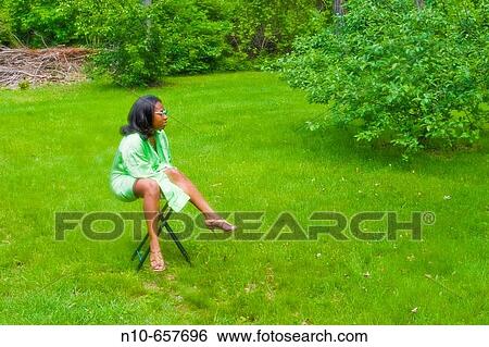 Young black woman, wearing sunglasses, sitting on a stool in her backyard. View Large Photo Image Stock Photograph - Young black woman, wearing sunglasses, sitting on a stool in her backyard.. Fotosearch