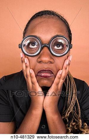 Stock Photo - Young black woman, with her hands on her face, wearing thick toy glasses. Fotosearch