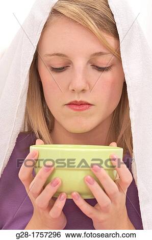Young blond woman holding a green bowl with hot water with a white towel over her head having an inhalation bath View Large Photo Image Stock Photograph - Young blond woman holding a green bowl with hot water with a white towel over her head having an inhalation bath. Fotosearch