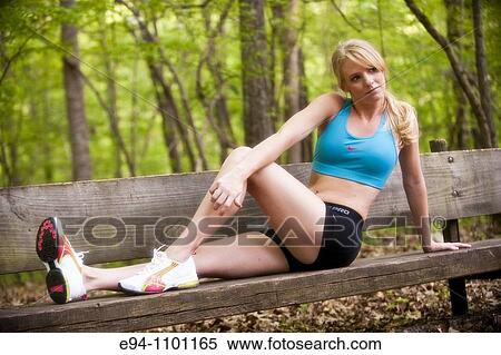 Stock Photography - Young blond woman looking away from camera in work out clothing sitting on a wooden bench in a park setting.. Fotosearch