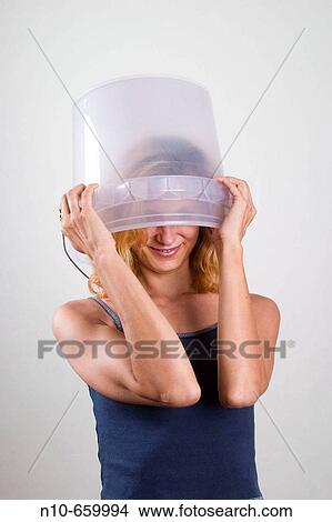 Picture - Young blond woman putting a clear bucket over her head.. Fotosearch