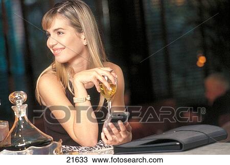 Stock Image - Young blond woman sitting in a bar with drink and electronic organizer. Fotosearch