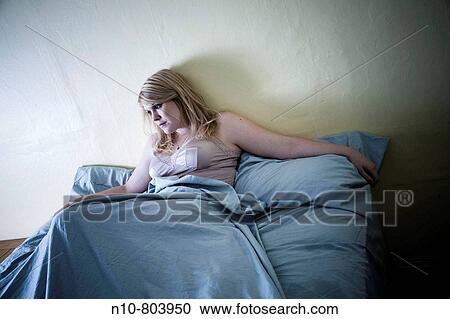 Stock Image - Young blond woman sitting on her bed.. Fotosearch