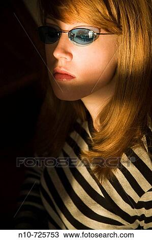 Stock Image - Young blond woman, wearing sunglasses, being lit by sunlight. Fotosearch