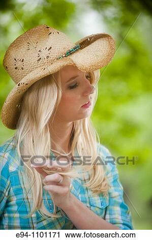 Stock Image - Young blond woman with a straw hat in a country outdoor setting looking away from camera.. Fotosearch