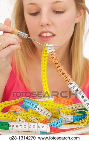 Young blond woman with long hair eating a colored tape out of a plate to evoke the concept of diet and weight problems, concept image View Large Photo Image Stock Image - Young blond woman with long hair eating a colored tape out of a plate to evoke the concept of diet and weight problems, concept image. Fotosearch