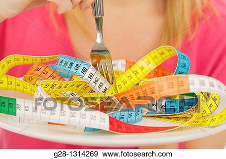 Young blond woman with long hair eating a colored tape out of a plate to evoke the concept of diet and weight problems, concept image detail View Large Photo Image Stock Photo - Young blond woman with long hair eating a colored tape out of a plate to evoke the concept of diet and weight problems, concept image detail. Fotosearch