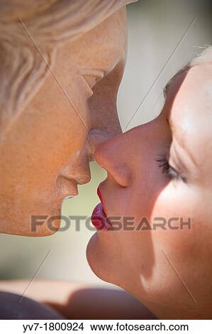 Picture - Young blonde girl kissing a sculpture. Fotosearch