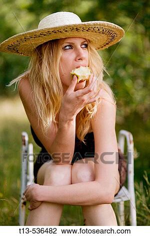 Young blonde woman eating apple sitting in green grass environment View Large Photo Image Stock Image - Young blonde woman eating apple sitting in green grass environment. Fotosearch