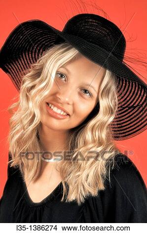 Young blonde woman in a black hat against a red background View Large Photo Image Picture - Young blonde woman in a black hat against a red background. Fotosearch