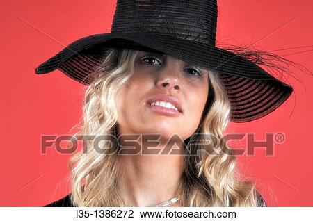Young blonde woman in a black hat against a red background View Large Photo Image Stock Image - Young blonde woman in a black hat against a red background. Fotosearch